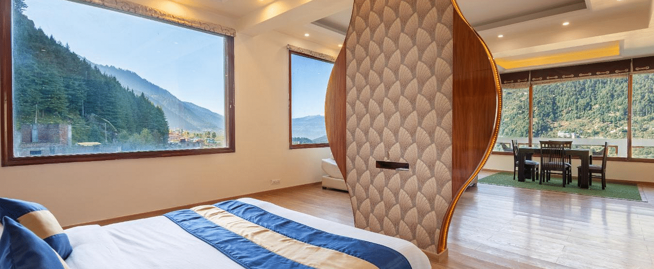 Shot of room with a king size bed, a partial view of a dining area, and large windows overlooking a scenic mountain landscape  | DLS Serenity Resort and Spa